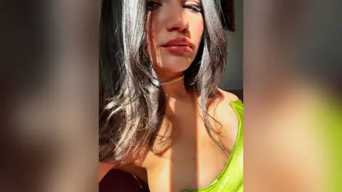 Young woman with long dark hair wearing a lime green top and pearl choker in warm sunlight.