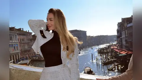 Stylish woman in a white tweed blazer posing by a scenic Venice canal on a sunny day.