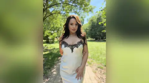 Elegant woman in a white lace slip dress posing in a sunny green park setting.