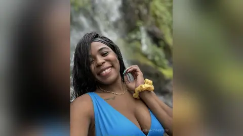 Smiling Black woman in a blue swimsuit enjoying a sunny day by a lush tropical waterfall.