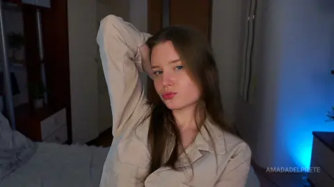Young woman in a beige linen shirt relaxing in a cozy, dimly lit bedroom setting.