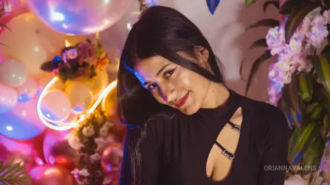 Smiling young woman in a black cutout top posing against colorful balloons and floral decorations.