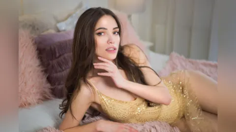 AlienaMoore — AlienaMoore lies on a bed with pink pillows wearing a gold sequined bodysuit.