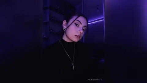 Young woman in a black turtleneck and silver necklace posing in moody purple ambient lighting.