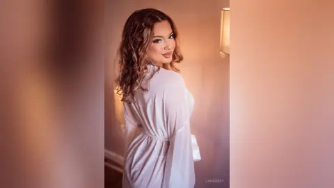 Elegant woman in a white silk robe posing with a soft, dreamy glow in a warm indoor setting.