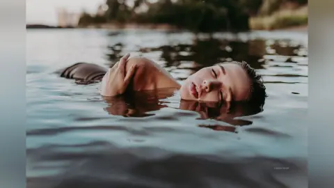 Serene woman floating in calm lake water during a peaceful sunset outdoor swim.