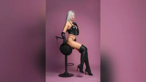 Glamorous blonde woman in black leather bodysuit and tall boots sitting on a stool against a purple background.
