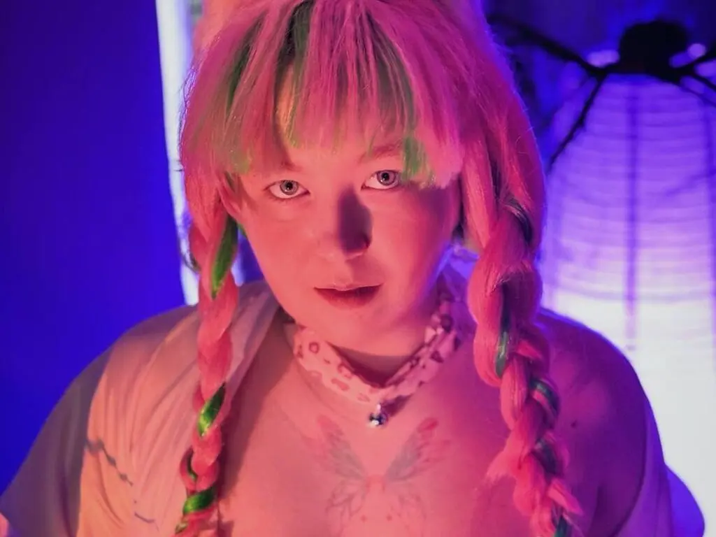 Woman with pink braided hair and butterfly tattoo posing in moody pink and blue neon lighting.