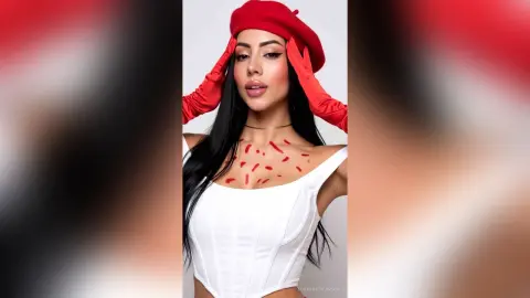 Glamorous woman in a white corset and red beret with red heart body art posing against a white background.