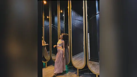 Elegant woman in a white crop top and pink sequin skirt posing in a luxury mirrored dressing room.