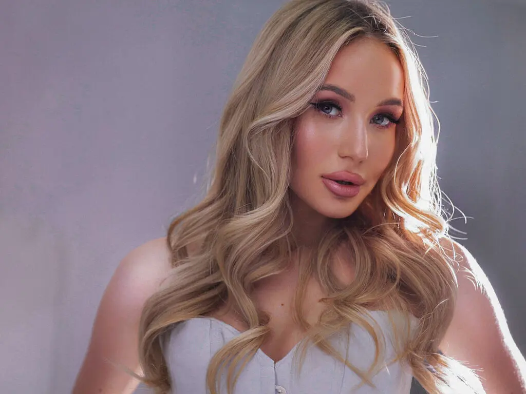 Glamorous blonde woman in a white strapless top with soft studio lighting and elegant wavy hair.
