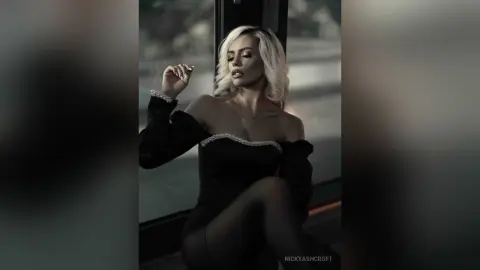 Elegant blonde woman in a black off-the-shoulder velvet dress posing gracefully in a moody, cinematic setting.