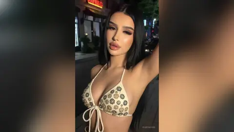 Glamorous woman in a cream floral bikini top posing outdoors at night with soft lighting.
