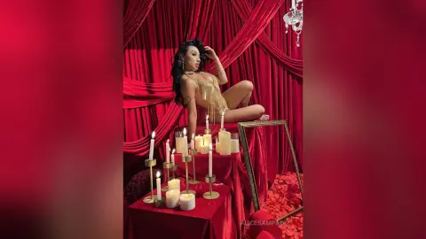 Glamorous woman in a gold sequin bodysuit posing amidst red velvet curtains and glowing candles.