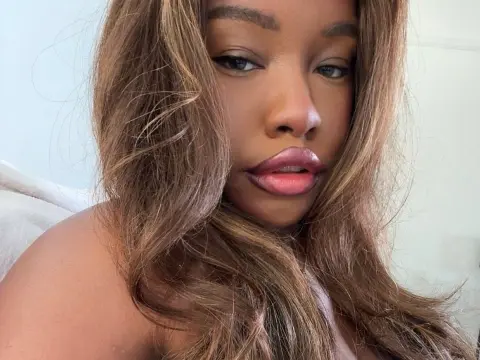 Close-up portrait of a beautiful Black woman with long wavy brown hair and pink lipstick in a soft indoor setting.