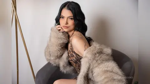 Glamorous woman in a leopard print top and fluffy faux fur coat sitting in a studio setting.