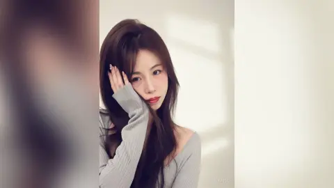 Young woman with long brown hair wearing a grey ribbed sweater in a bright, minimalist indoor setting.