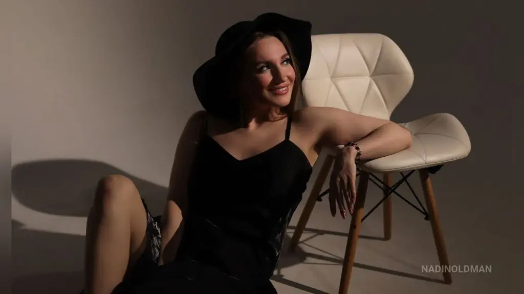 Young woman with dark hair in a black camisole posing against a dark backdrop with moody lighting.