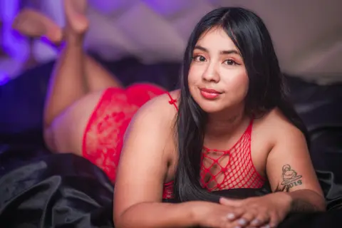 Curvy woman in red lace lingerie relaxing on black satin sheets in a moody, intimate bedroom setting.
