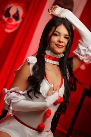 EmilyyJhonson wears a white and red clown costume with ruffled sleeves while posing against a red background.