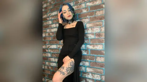 Blue-haired woman in a black long-sleeve top and skirt posing against a rustic brick wall with a moody vibe.