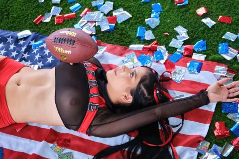 Young woman in red outfit lying on American flag with confetti for a patriotic celebration mood.