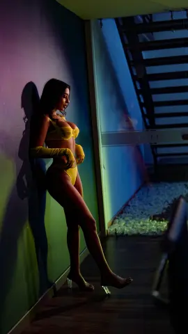 Woman in yellow lingerie and gloves leaning against a wall in moody, cinematic blue lighting.