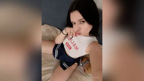 Young woman in a white Malibu graphic tee and navy shorts relaxing on a bed with a playful expression.