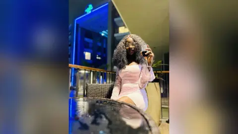 Stylish woman in a pink dress enjoying red wine on a rooftop balcony at night under blue city lights.