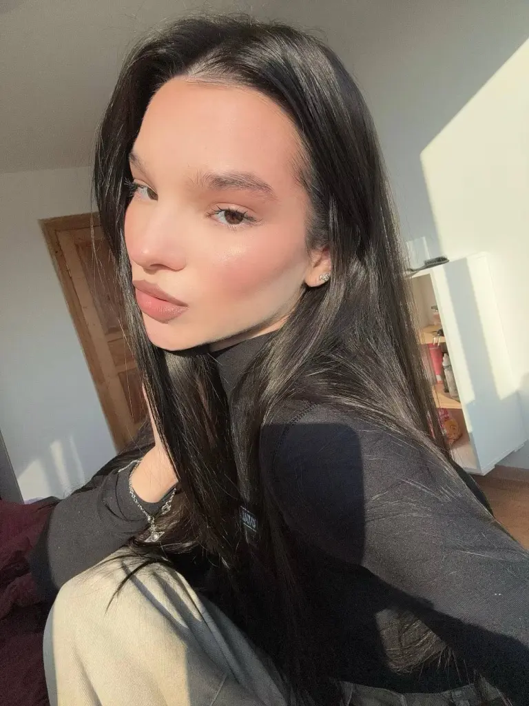 Noirbeauty looks into the camera with long dark hair and sunlit skin in a close-up shot.