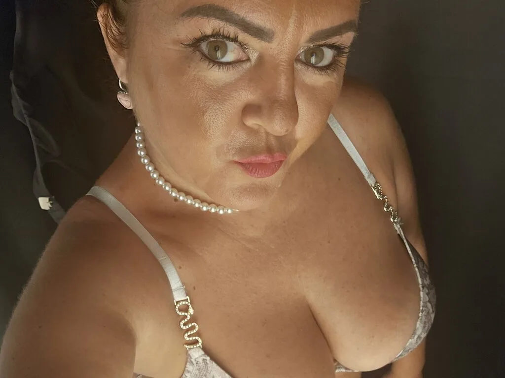 AngelaDaysy wears a white lace bra and pearl necklace while looking into the camera.