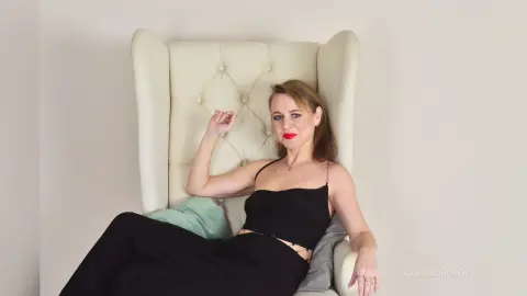GabrielMoren reclines in a white tufted wingback chair wearing a black tank top and black pants.
