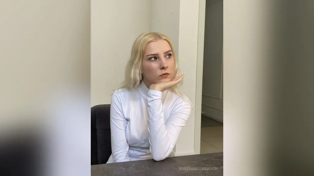 Blonde woman in a white turtleneck looking thoughtfully away in a bright indoor setting.