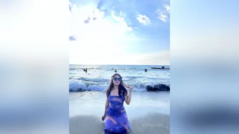 Young woman in a blue summer dress enjoying a sunny day on a tropical beach with ocean waves.