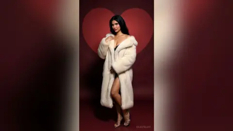 Elegant woman in a luxurious white faux fur coat posing against a romantic red heart backdrop.