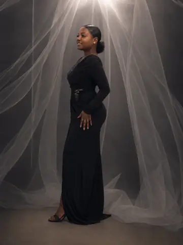 LilyReeds poses in a long black dress against a backdrop of flowing white sheer fabric.