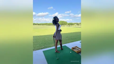 Smiling Black woman in a white tank top and brown skirt playing golf on a sunny green course.