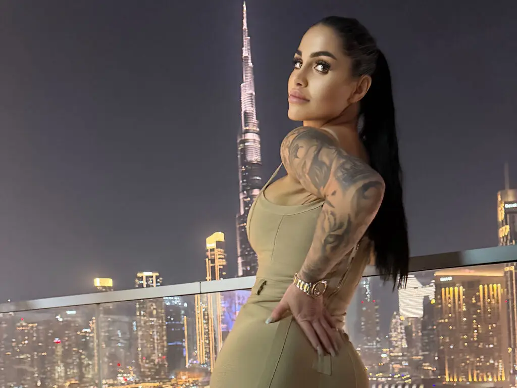 Glamorous woman in a beige dress posing on a rooftop overlooking the Burj Khalifa skyline at night.