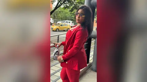 Stylish woman in a red blazer and sunglasses standing outdoors near a street with a confident mood.