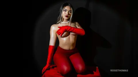 Glamorous woman in red gloves and leggings posing against a dark studio background with dramatic lighting.