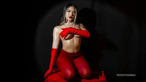 RosieThomas — Glamorous woman in red gloves and leggings posing against a dark studio background with dramatic lighting.
