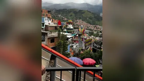 Panoramic view of a colorful hillside town in Colombia under a cloudy sky with a large statue overlooking the city.