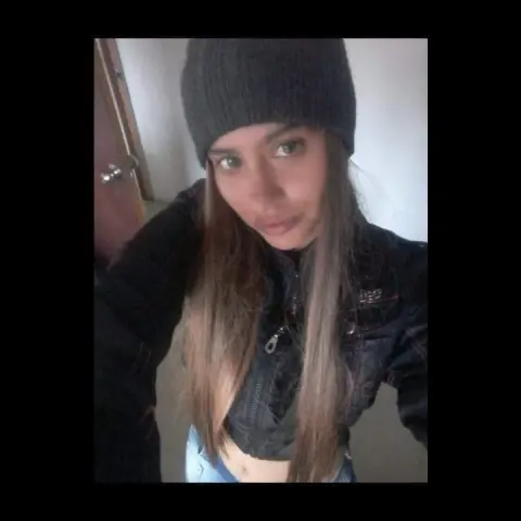 SilvannaReed wears a dark beanie and a black jacket, looking directly at the camera with long brown hair falling over her shoulders.