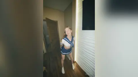 Young woman in a blue and white sailor outfit posing in a modern minimalist room with soft lighting.