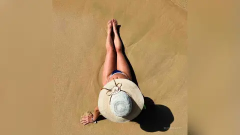 Woman in a white bikini and straw hat relaxing on a sunny sandy beach.