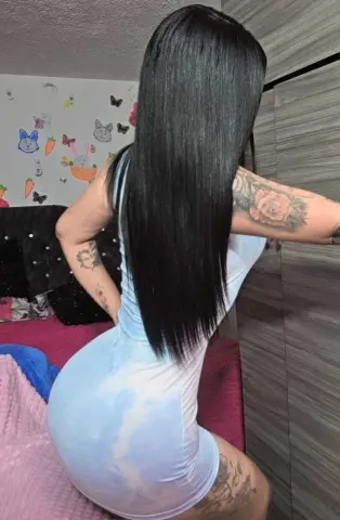 Woman with long straight black hair wearing a tight white mini dress in a bedroom setting.