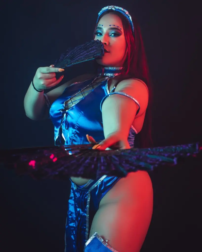 NaomyEvanss poses in a blue shiny top and headpiece, showing her face and shoulders against a dark background.