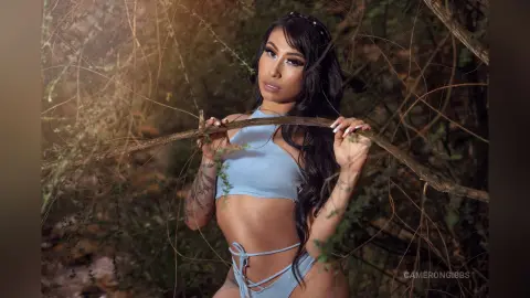 Beautiful woman in a light blue bikini posing amidst lush forest greenery in a dreamy, natural setting.