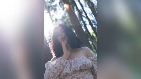 Dreamy portrait of a woman in a floral off-the-shoulder blouse amidst a sunlit, misty forest setting.