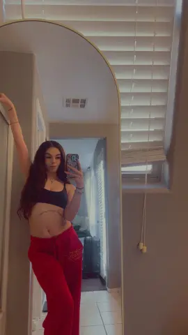 Young woman in black crop top and red sweatpants taking a mirror selfie in a bright bedroom.